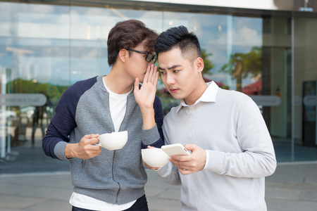 Closeup portrait of guy whispering into man's ear telling him something secretの写真素材