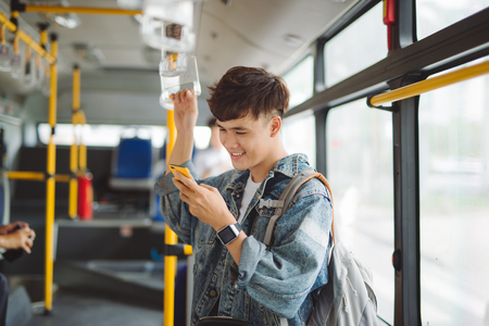 Handsome asian man sitting in city bus and typing a message on the phone.の写真素材