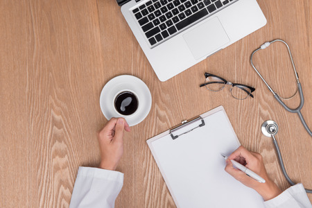 Top view of adult doctor working with clipboard on his desk and holding penの写真素材