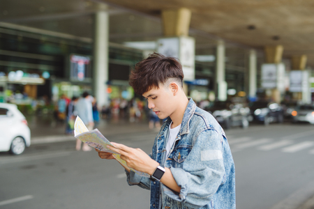 Asian male tourist reading map while waiting for taxi at the airportの写真素材