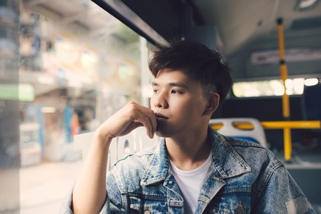 Asian man traveler contemplating outdoor view from window of train or bus.の写真素材