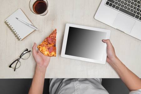 Man holding a digital tablet and tasty pizza with ingredients on wooden table.の写真素材