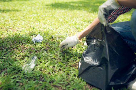 Young man crouching to waste and picking it up in bin bagの写真素材