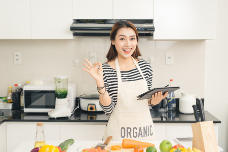 Beautiful young housewife woman with tablet computer cooking in a kitchenの写真素材