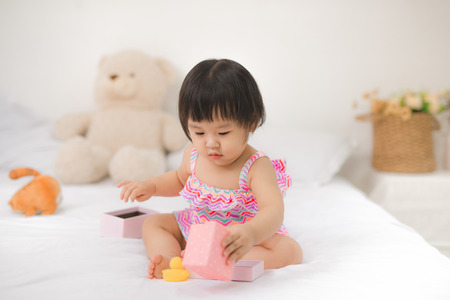 Little cute asian baby girl sitting on bed playingの写真素材