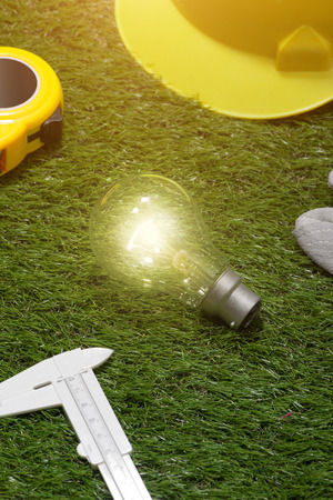 House engineer and architect ideas concept with light bulb. Yellow hat and tools on green grass backgroundの写真素材