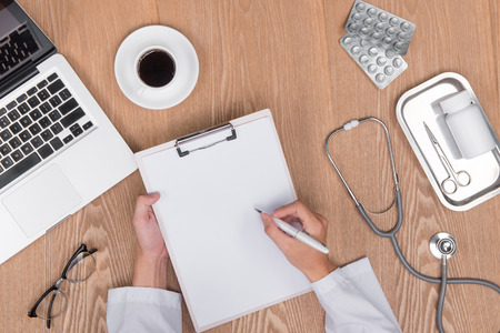 Top view of adult doctor working with clipboard on his desk and holding penの写真素材