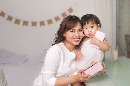 Happy family, beautiful young mother with her adorable little daughter open gift box