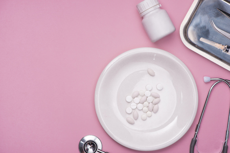 Pills served as a healthy meal. Drug capsule on white plate on pink backgroundの写真素材