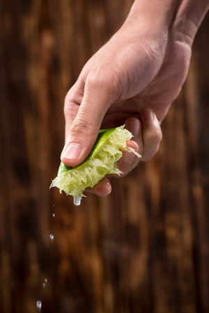 Hand squeeze lime with lime drop on dark wooden backgroundの写真素材
