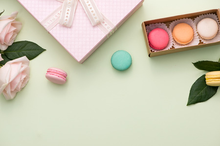 French macaroons. Many variegated sweet macarons in box with bouquet of pink roses on the tableの写真素材