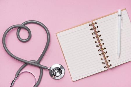Medical concept. The stethoscope with heart shape and open notebook on pink background.の写真素材