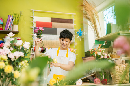 Smiling young asian florist man making bunch at flower shopの写真素材
