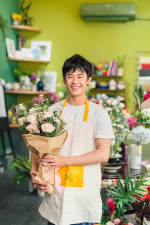 Handsome male florist is standing in flower shop and holding bouquet of flowersの写真素材