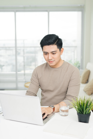 Portrait of a casual smiling young man using laptop at homeの写真素材