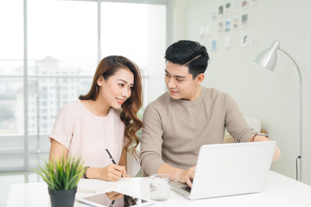 Happy young couple reading and analyzing bills sitting at table. Young couple in casual discussing home economicsの写真素材