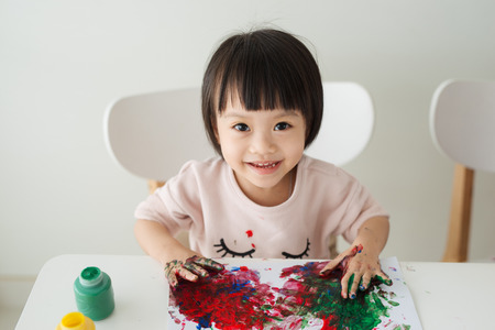 Little asian girl painting with paintbrush and colorful paintsの写真素材