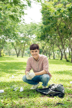 Young man crouching to waste and picking it up in bin bagの写真素材