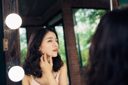 Beauty, skin care lifestyle concept. Young asian woman with acne looking at the mirror.の写真素材