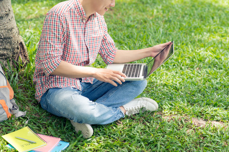 Cropped image of student sitting on the green grass and working on laptopの写真素材