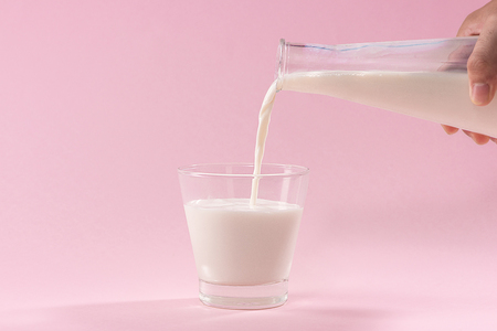 Pouring milk in to glass from bottle on a pinkの写真素材