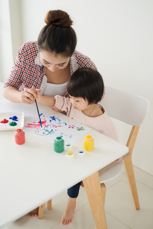 Happy family mother and daughter together paint. Asian woman helps her child girl.の写真素材