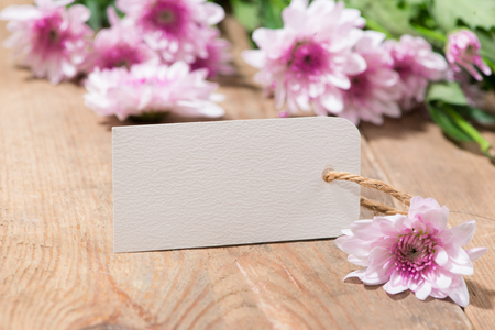 Blank white tag paper with color flowers on wooden background. Top view. Mock upの写真素材
