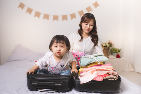 Asian mom and baby girl with suitcase baggage and clothes ready for traveling on vacationの写真素材