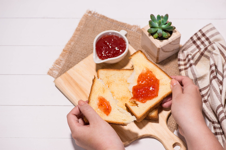 Woman hands eating bread with strawberry jam for breakfast. Focus on hands.の写真素材