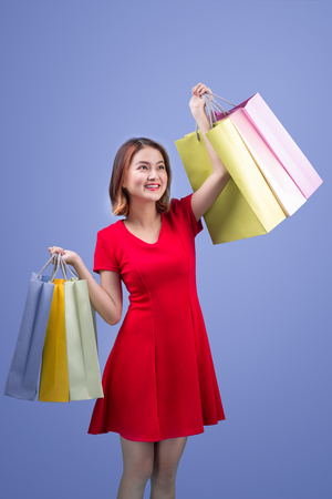 Beautiful young asian woman with colored shopping bags over violet backgroundの写真素材