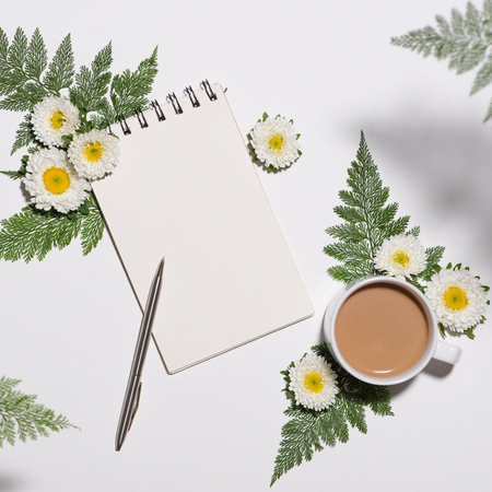 Flat lay of green leaves and flowers pattern with cup of coffee and paper note on white backgroundの写真素材