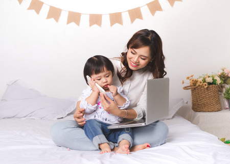 Asian lady in classic suitvworking on laptop at home with her baby girl chatting with father.の写真素材