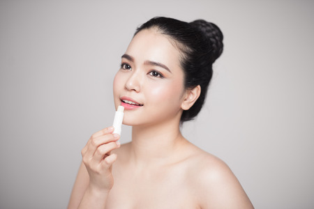 Asian woman applying hygienic lip balm over grey backgroundの写真素材