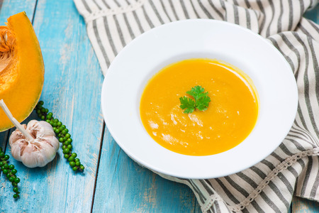 Pumpkin and carrot soup with cream and parsley on blue  wooden background.の写真素材