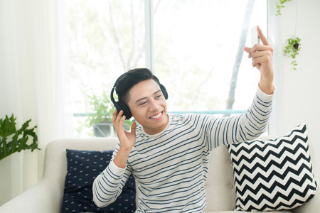 Young man relaxing on sofa with headphones in the living room.の写真素材