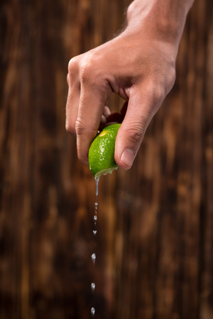 Hand squeeze lime with lime drop on dark wooden backgroundの写真素材