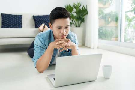 Asian man lying on the floor with laptop and coffee.の写真素材