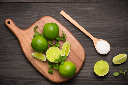 Fresh limes on cutting board on wooden table with spoon of salt. Top view, background.の写真素材