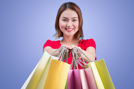 Beautiful young asian woman with colored shopping bags over violet backgroundの写真素材