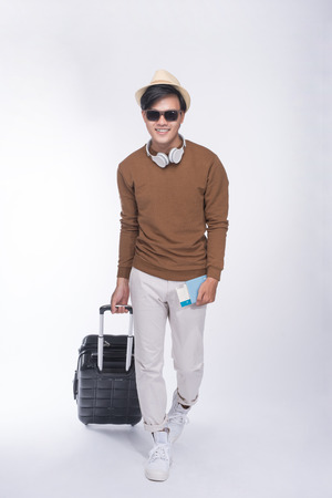 Full length of young tourist asian man holding passport with suitcase over grey backgroundの写真素材