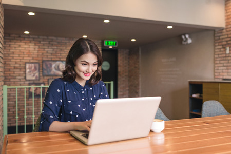 Beautiful cute asian young businesswoman in the cafe, using laptop and drinking coffee smilingの写真素材