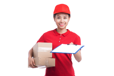 Beautiful young delivery woman in red t-shirt and cap smiling, holding a folder and making notes, on white backgroundの写真素材