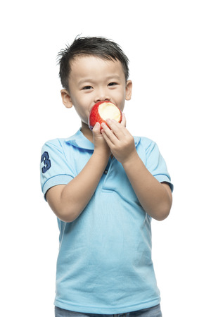 Asian baby boy holding and eating red apple, isolated on whiteの写真素材