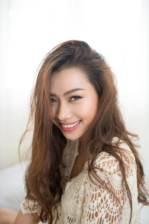 Asian woman breathing and sitting on a bed at home with a window in the backgroundの写真素材