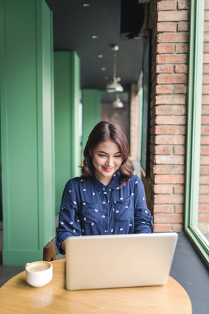Beautiful cute asian young businesswoman in the cafe, using laptop and drinking coffee smilingの写真素材