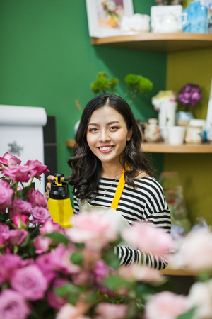 Young beautiful asian girl florist taking care of flowers at workplace.の写真素材