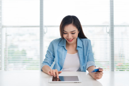 Woman sitting in modern home office and using credit card for paying over tablet deviceの写真素材