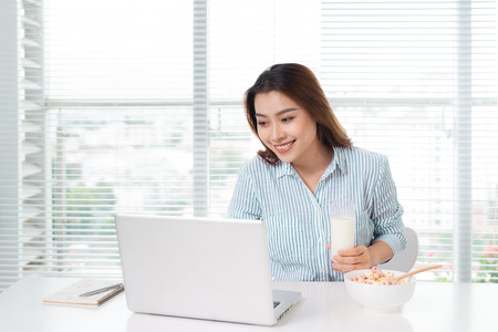Young attractive asian businesswoman drinking milk while sitting at office deskの写真素材