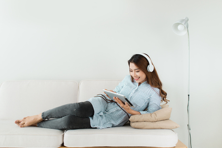 Pretty asian listening to music on couch at home in the living roomの写真素材