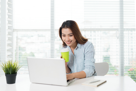 Young confident businesswoman working at office desk and typing with a laptopの写真素材